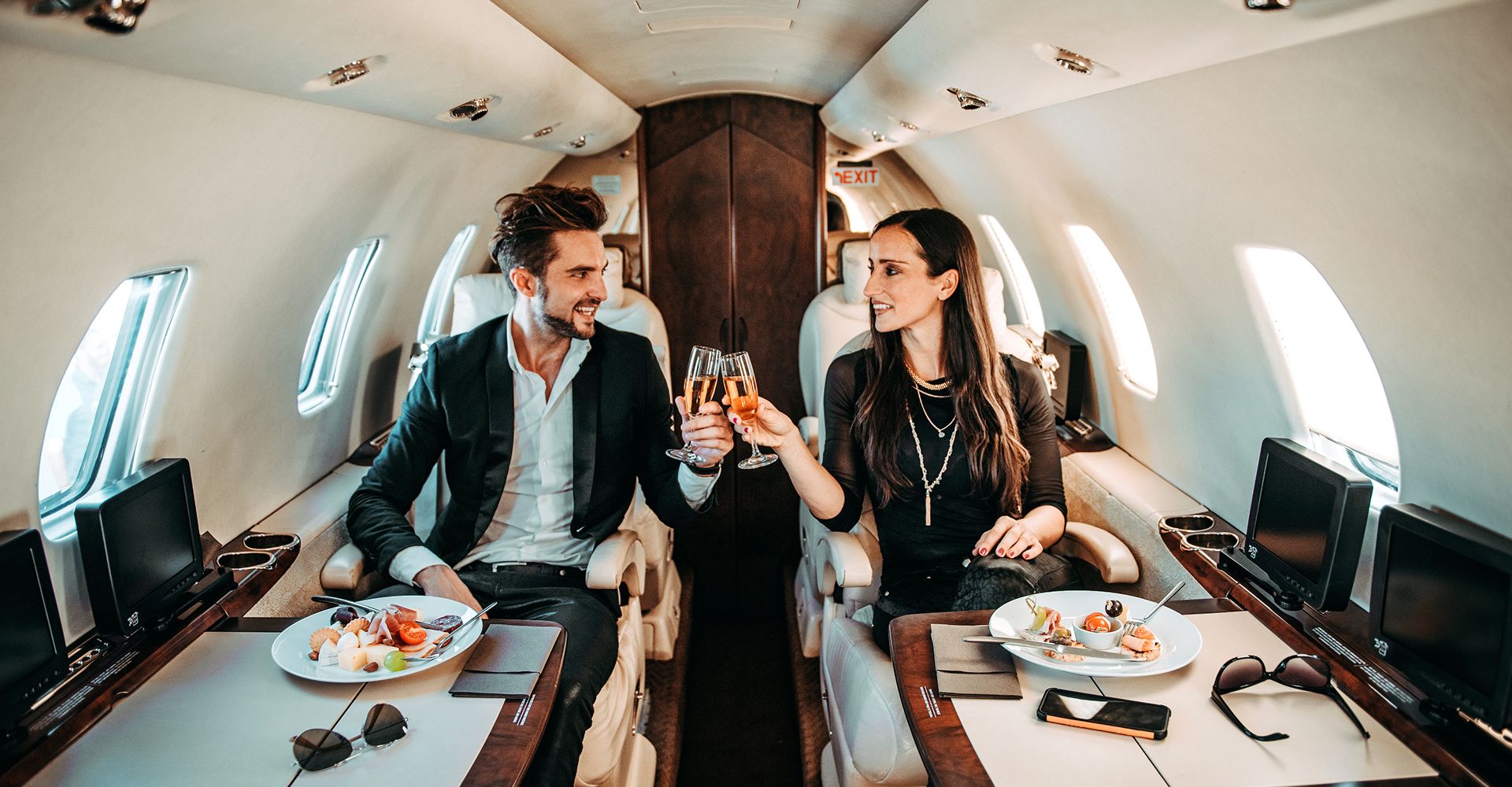 A well-dressed couple toasts champagne while seated in a private jet.