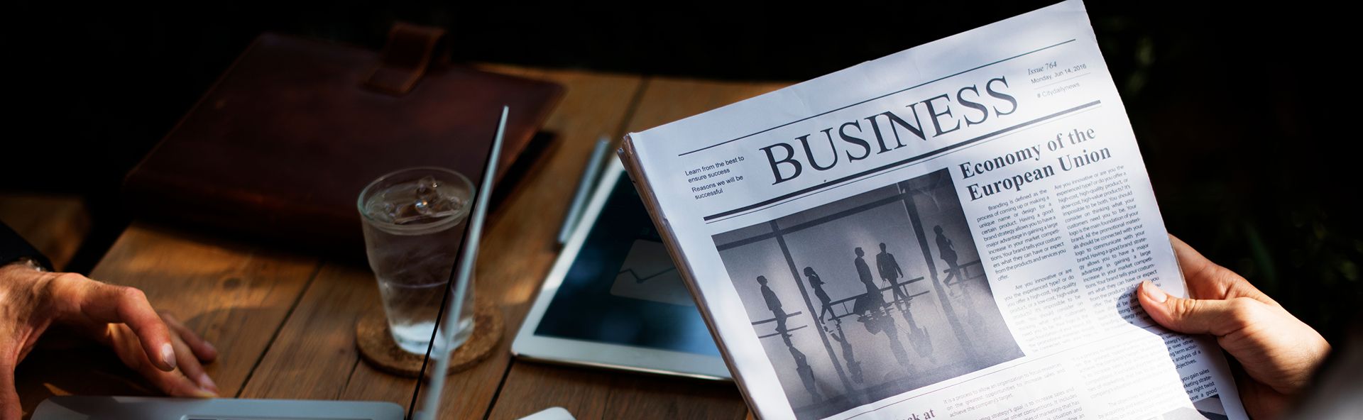 Person holding a newspaper with the headline "BUSINESS" above a photograph.